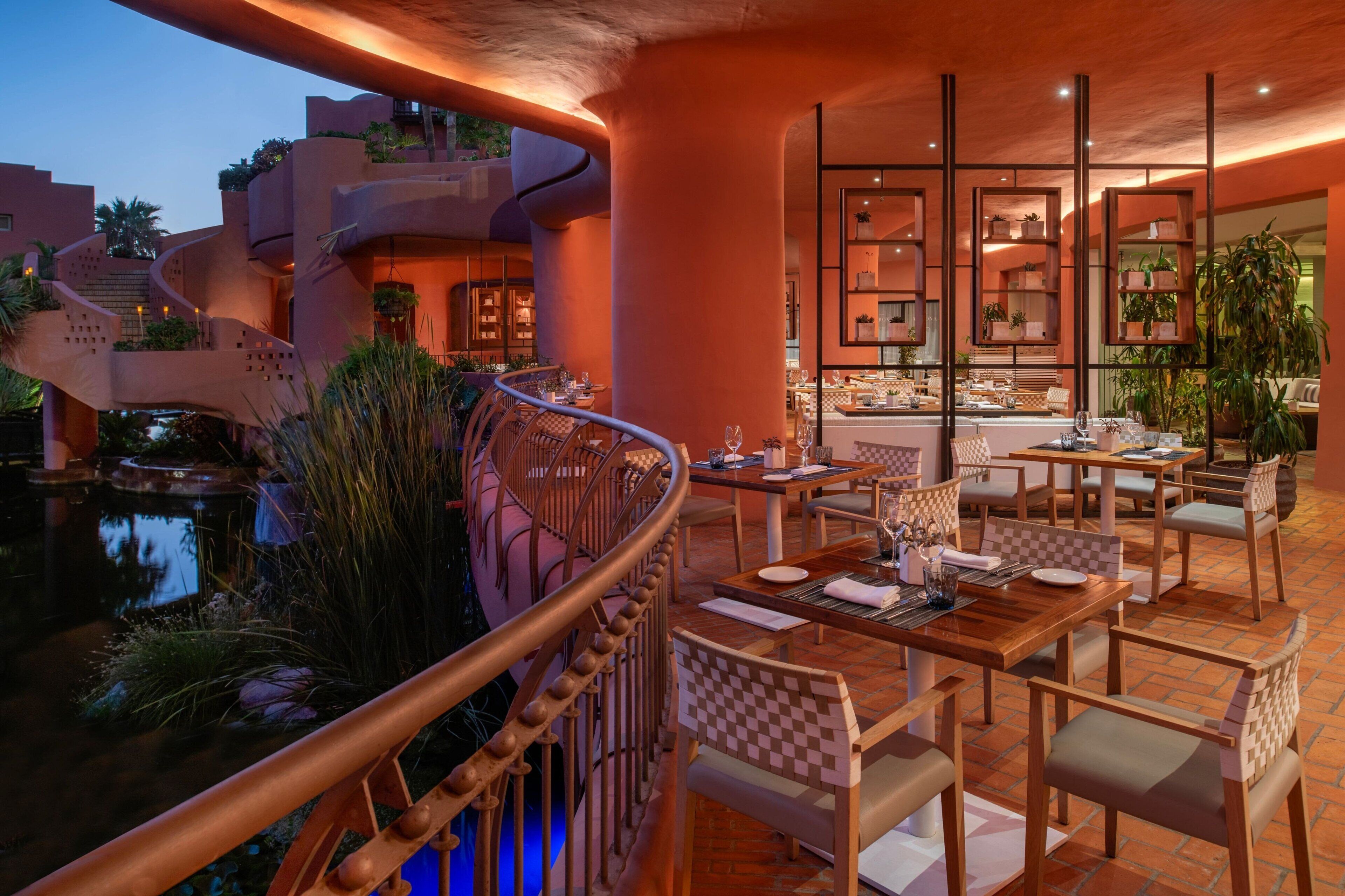 A dining area with outdoor seating, a pool, and a staircase leading to upper levels.