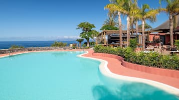 Piscina de resort con borde curvo, rodeada de palmeras y vista al océano.