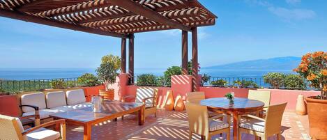Eine Terrasse im Freien mit einer Holzpergola, Korbmöbeln und Blick aufs Meer.