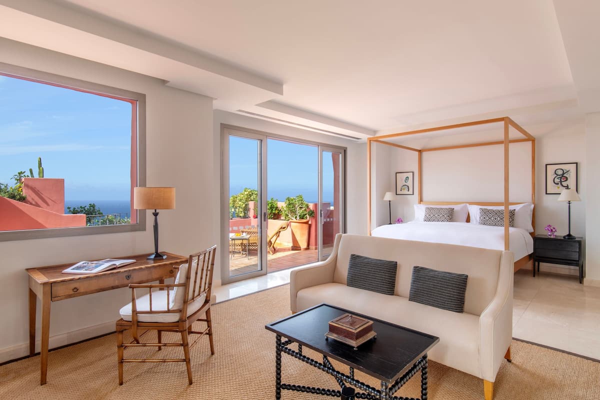 Habitación de hotel con una cama grande, un escritorio, una silla, una mesita de café y vista al océano.