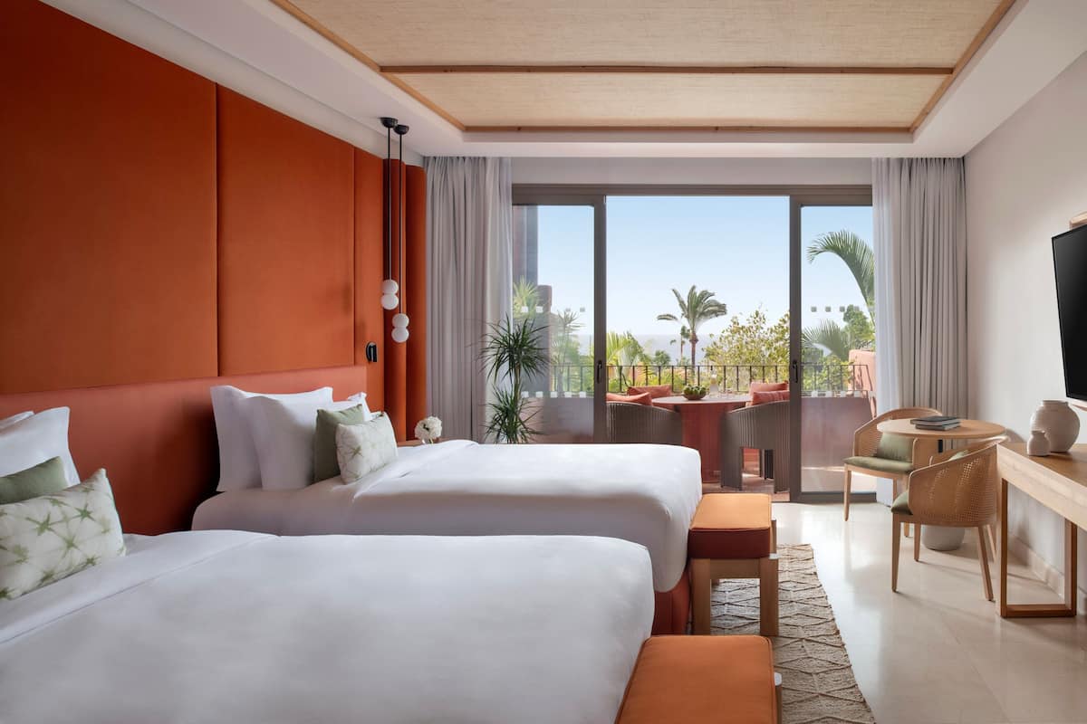 Una habitación de hotel con dos camas, un balcón con vistas, un escritorio y un televisor.