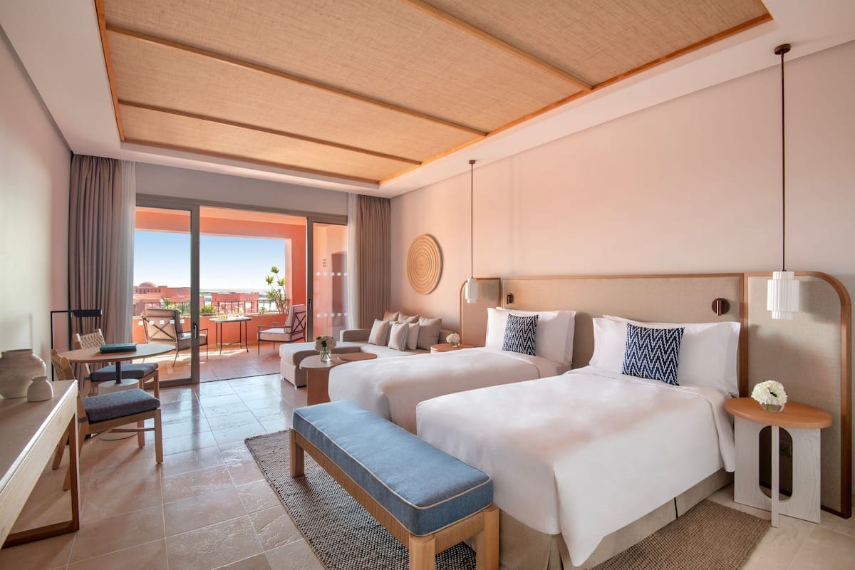 Habitación de hotel con dos camas, un escritorio y un balcón con vistas.