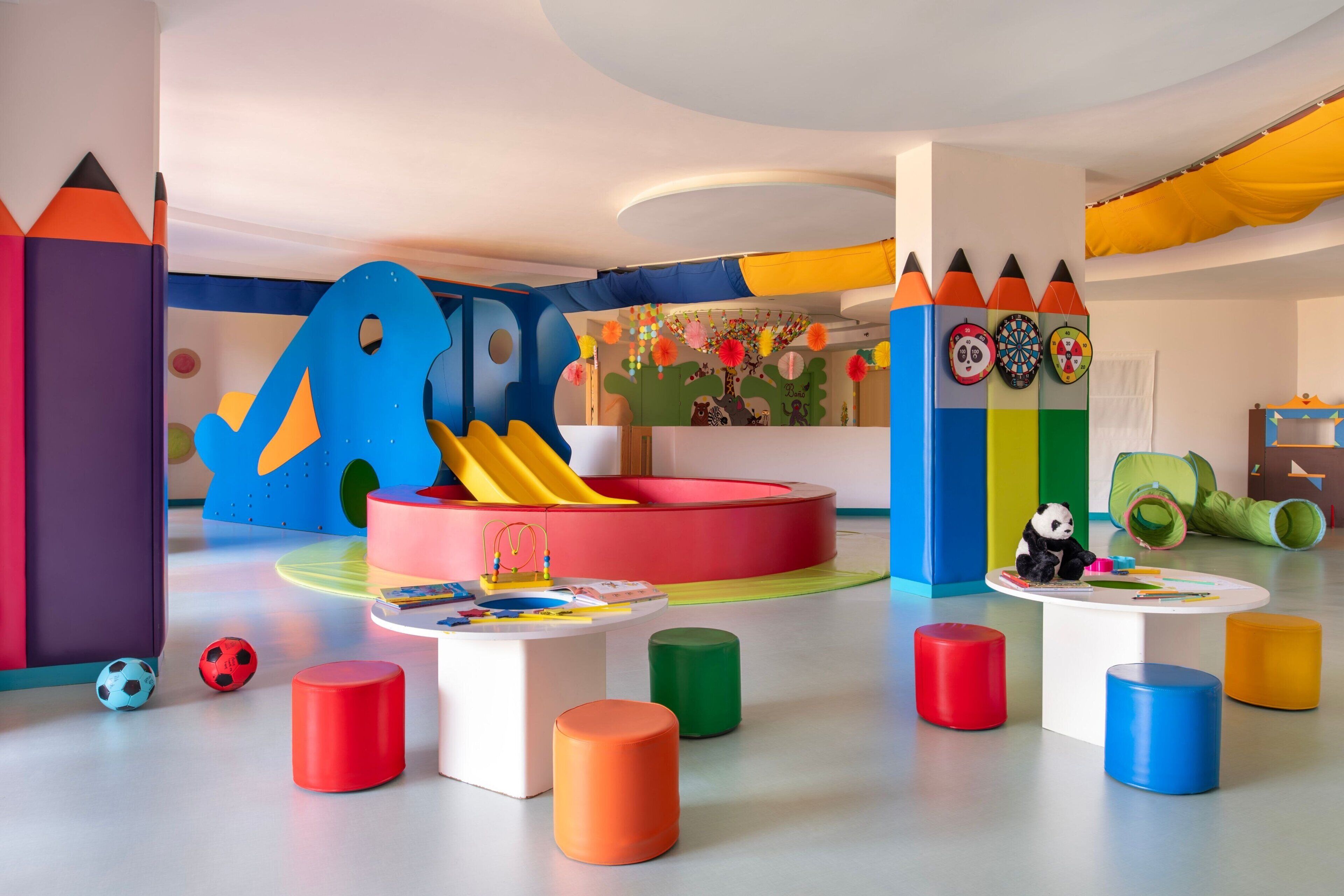 A playroom with colorful furniture, a slide, and a panda decoration.