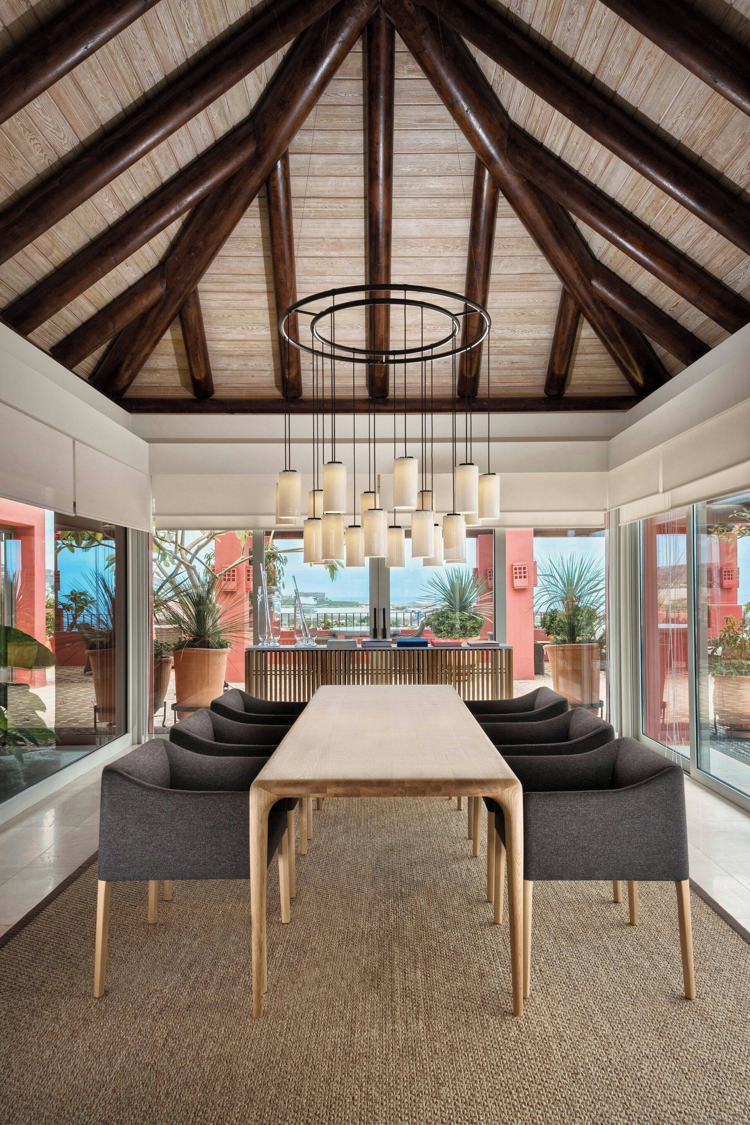 A modern dining area with a high ceiling, wooden beams, and a central table with chairs.