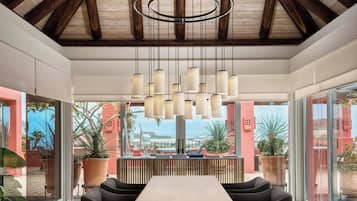 A modern dining area with a high ceiling, wooden beams, and a central table with chairs.