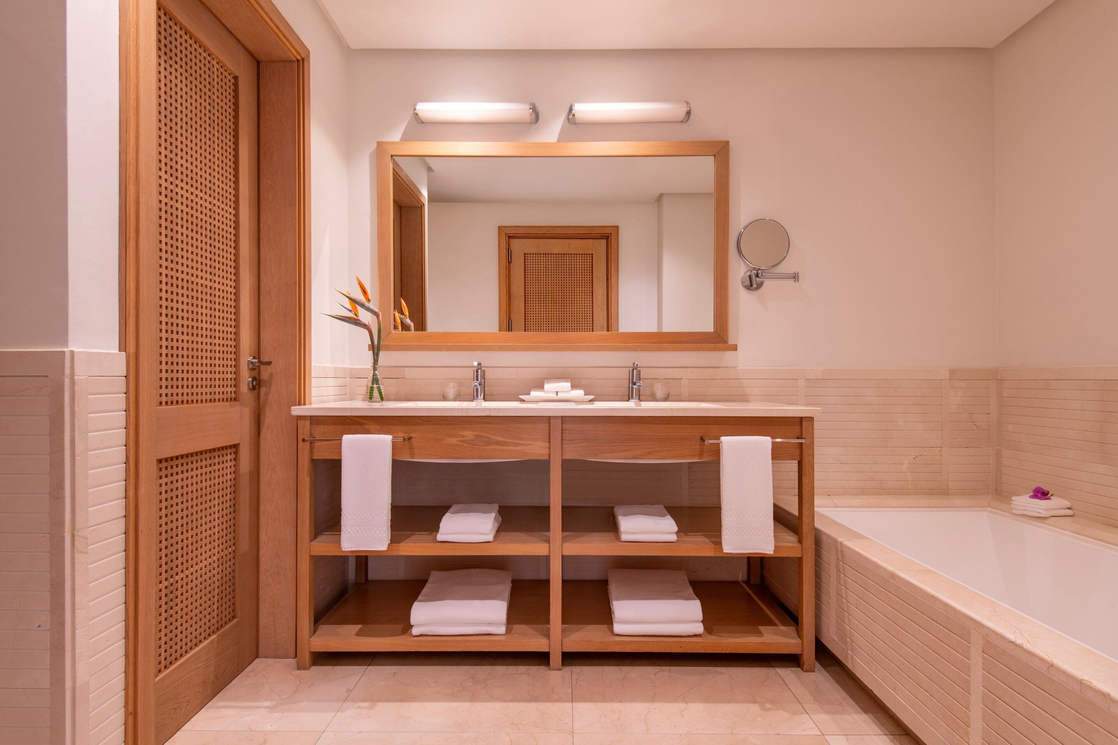 Un baño con tocador de madera, dos lavamanos, un espejo grande y una bañera.