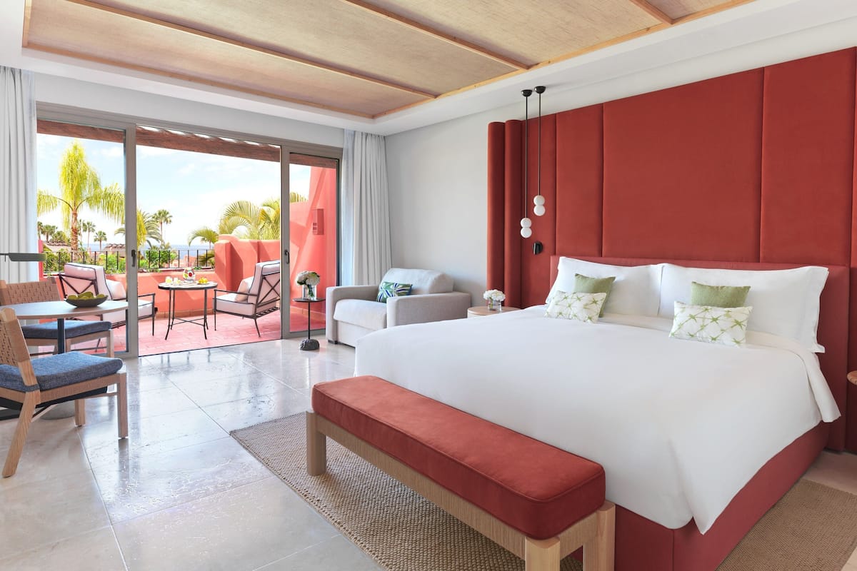 Un dormitorio amplio con una cama grande, un banco y una zona de estar con vistas al exterior.