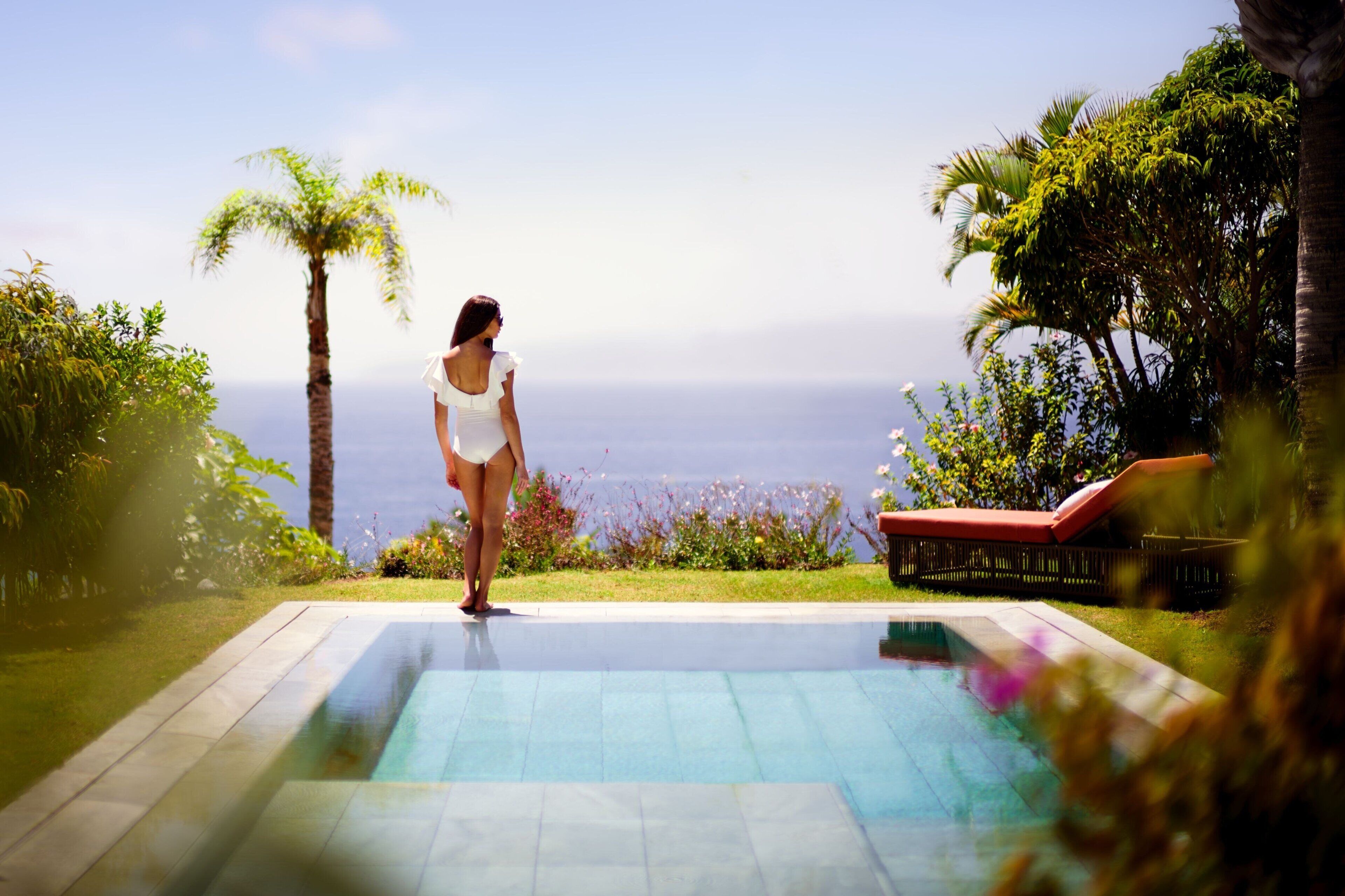 A woman standing at the edge of a swimming pool with a view of the ocean.