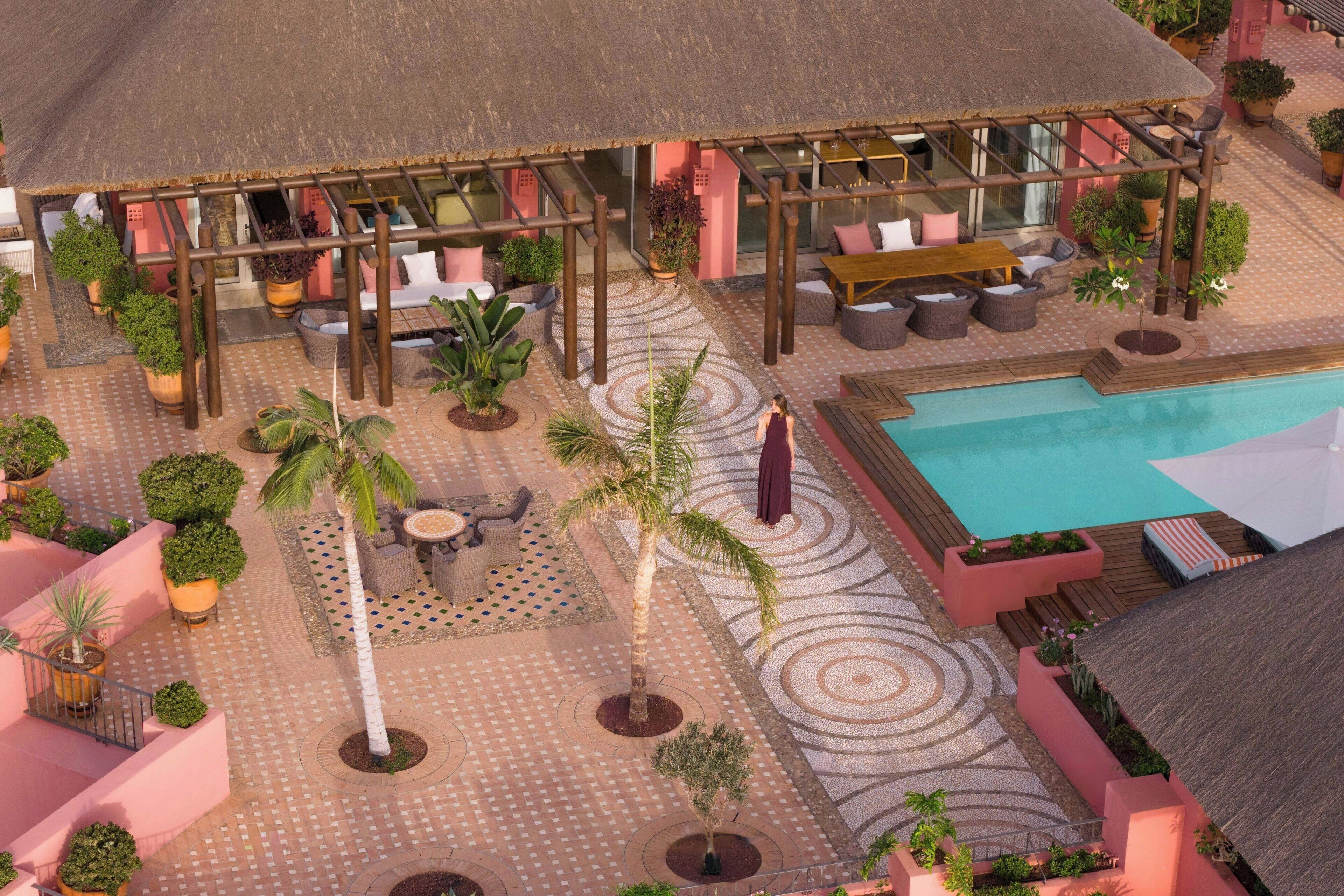 A rooftop pool area with lounge seating, palm trees, and a thatched roof structure.