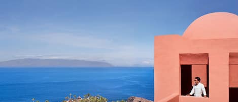 A coastal view with a person on a balcony overlooking the ocean and a town below.