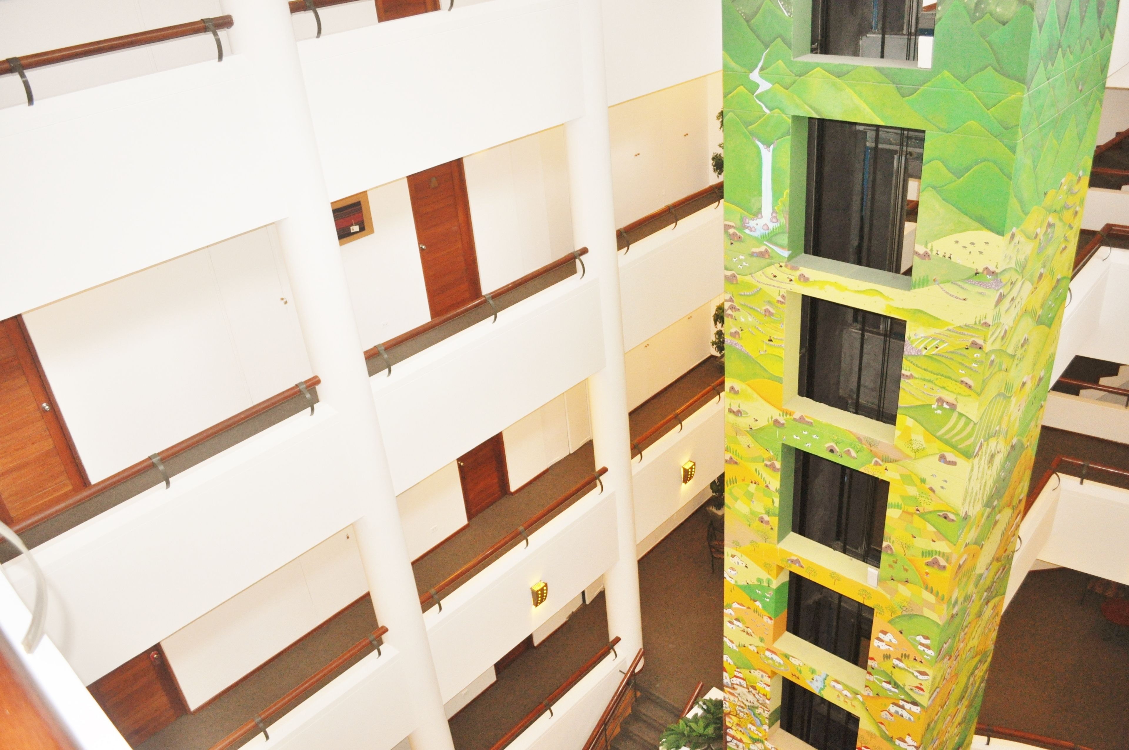 A multi-story building with a central atrium, wooden railings, and a colorful mural on one side.