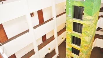 Ein mehrstöckiges Gebäude mit einem zentralen Atrium, Holzgeländern und einem farbenfrohen Wandgemälde an einer Seite.