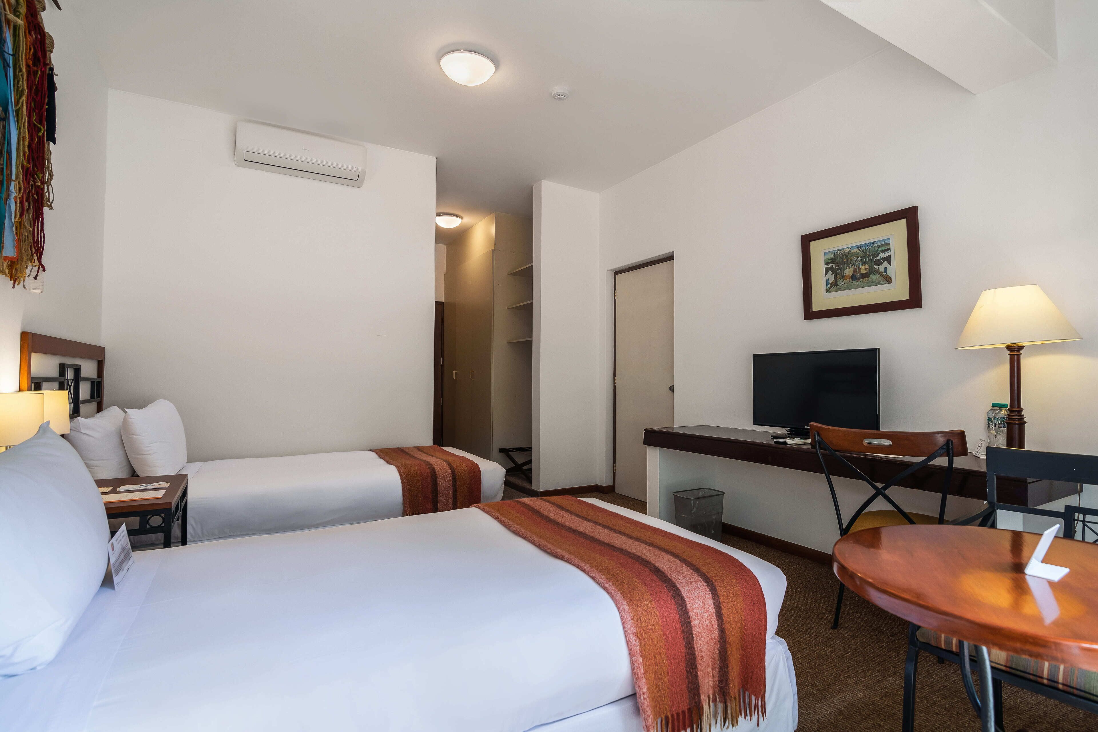 Een hotelkamer met twee bedden, een bureau, een televisie en een eettafel.
