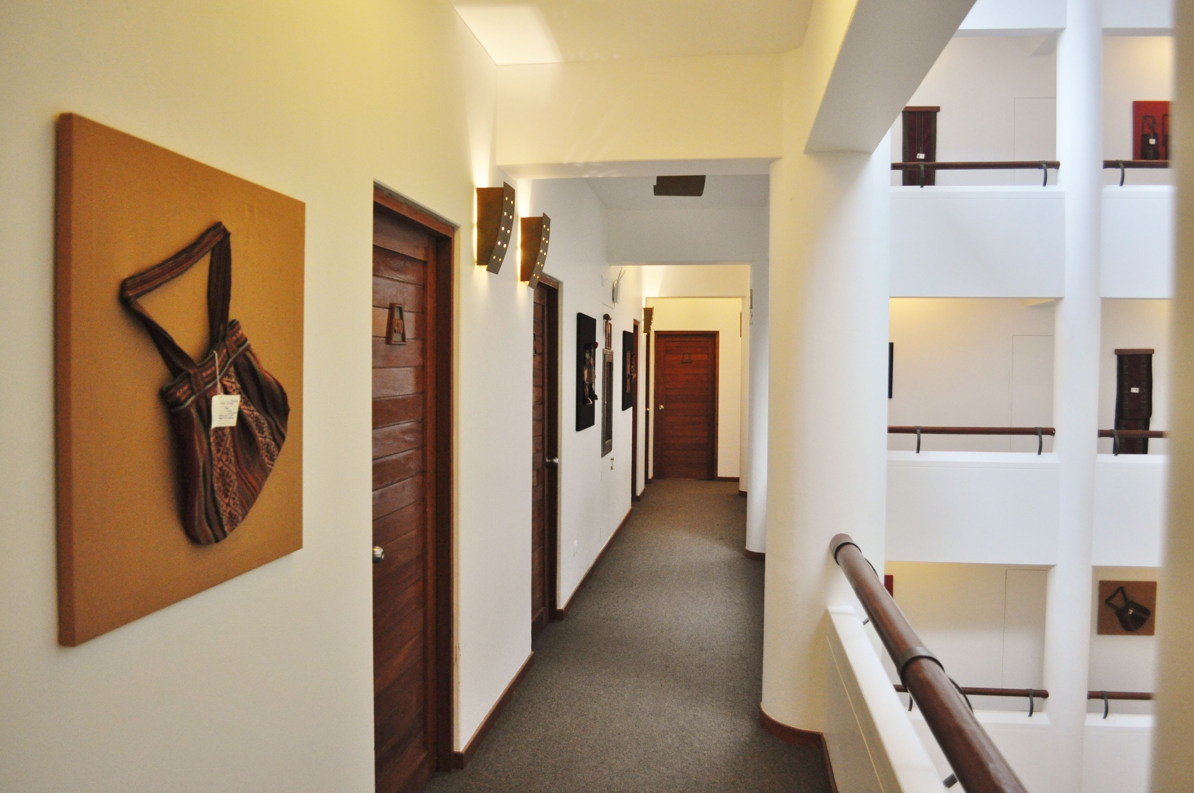 A hotel corridor with wooden doors, a staircase, and a view of the upper floor.