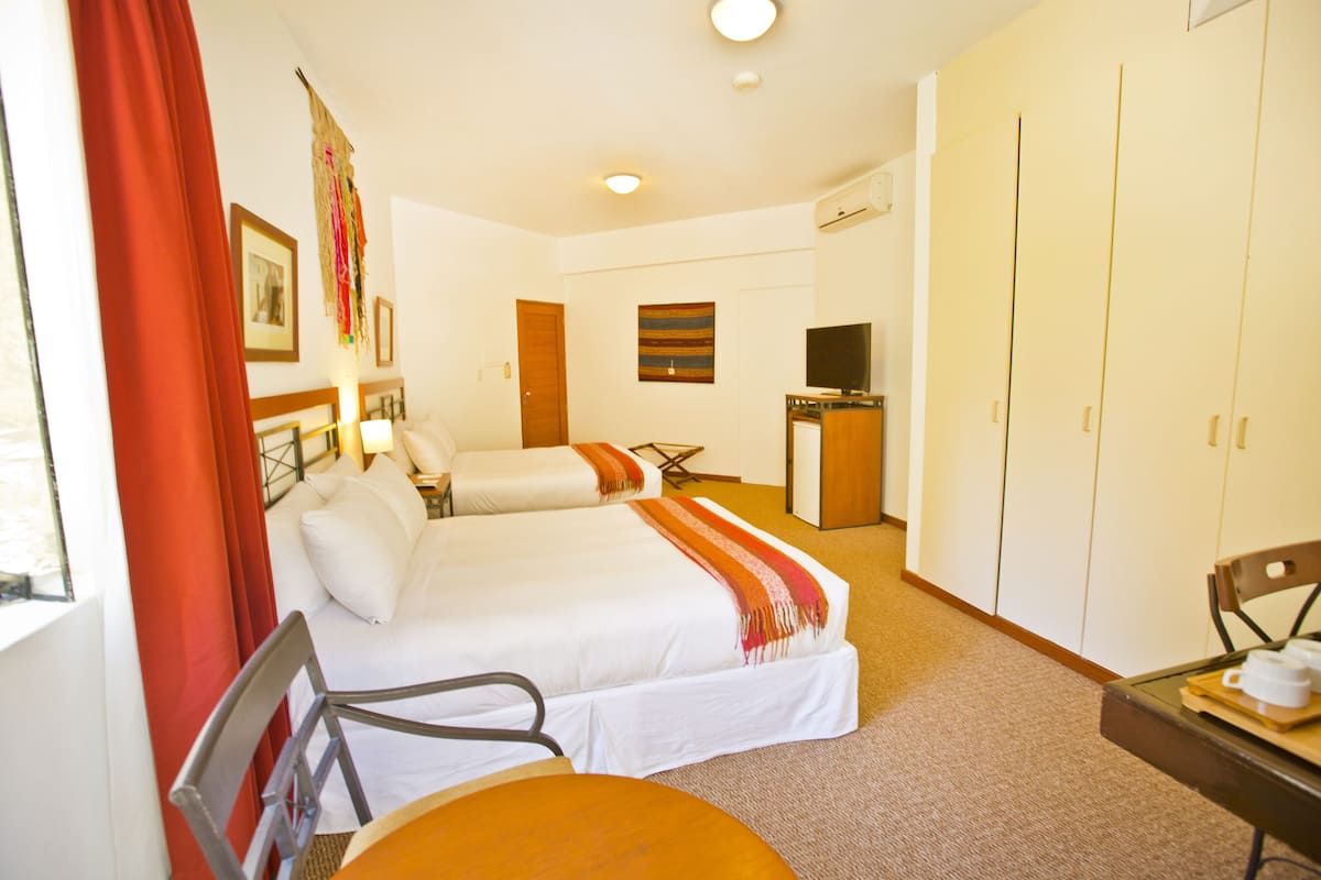 A hotel room with two beds, a desk, a chair, a television, and a wardrobe.