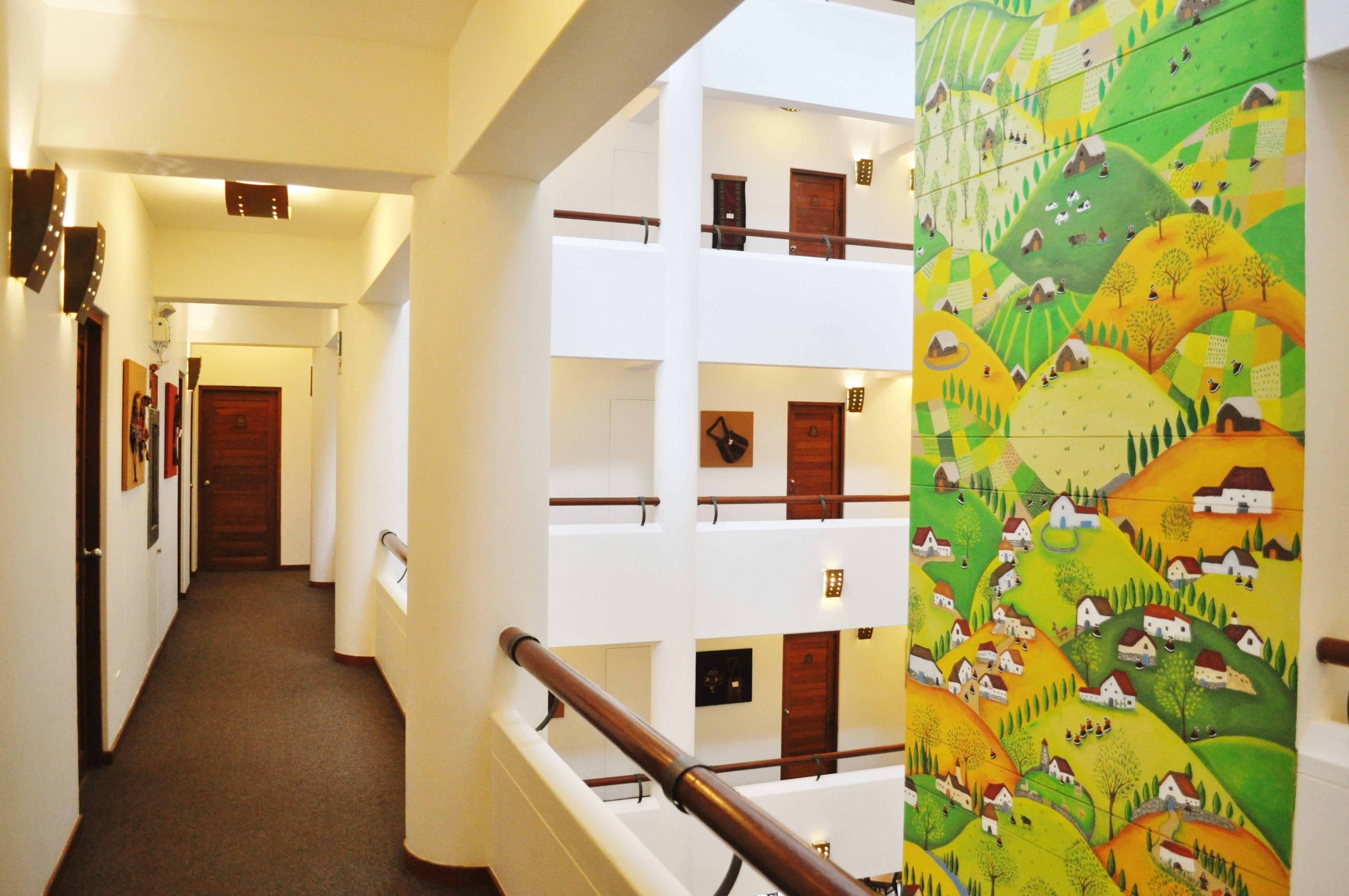 A multi-level hotel interior with a central staircase, multiple floors, and a vibrant mural on one wall.