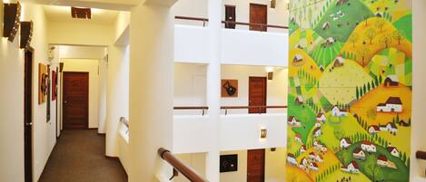 A multi-level hotel interior with a central staircase, multiple floors, and a vibrant mural on one wall.