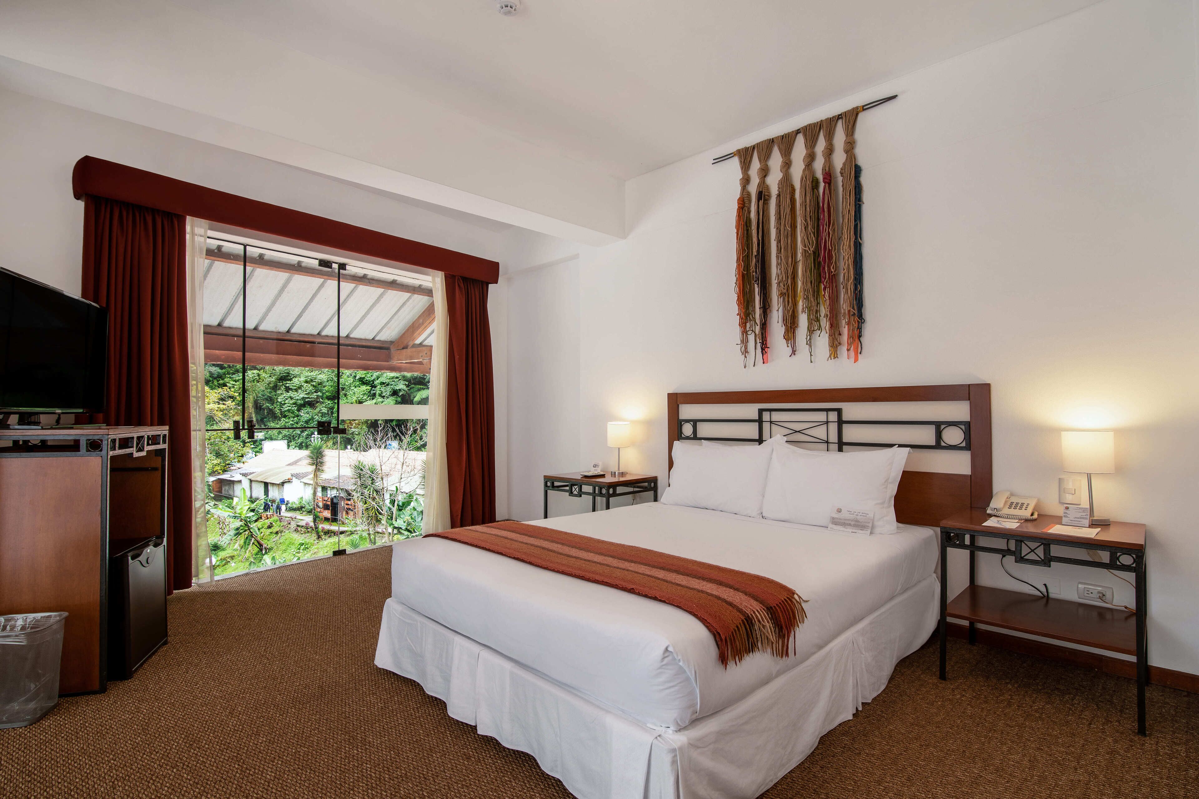 A hotel room with a large bed, a TV, a desk, and a view of the outdoors.