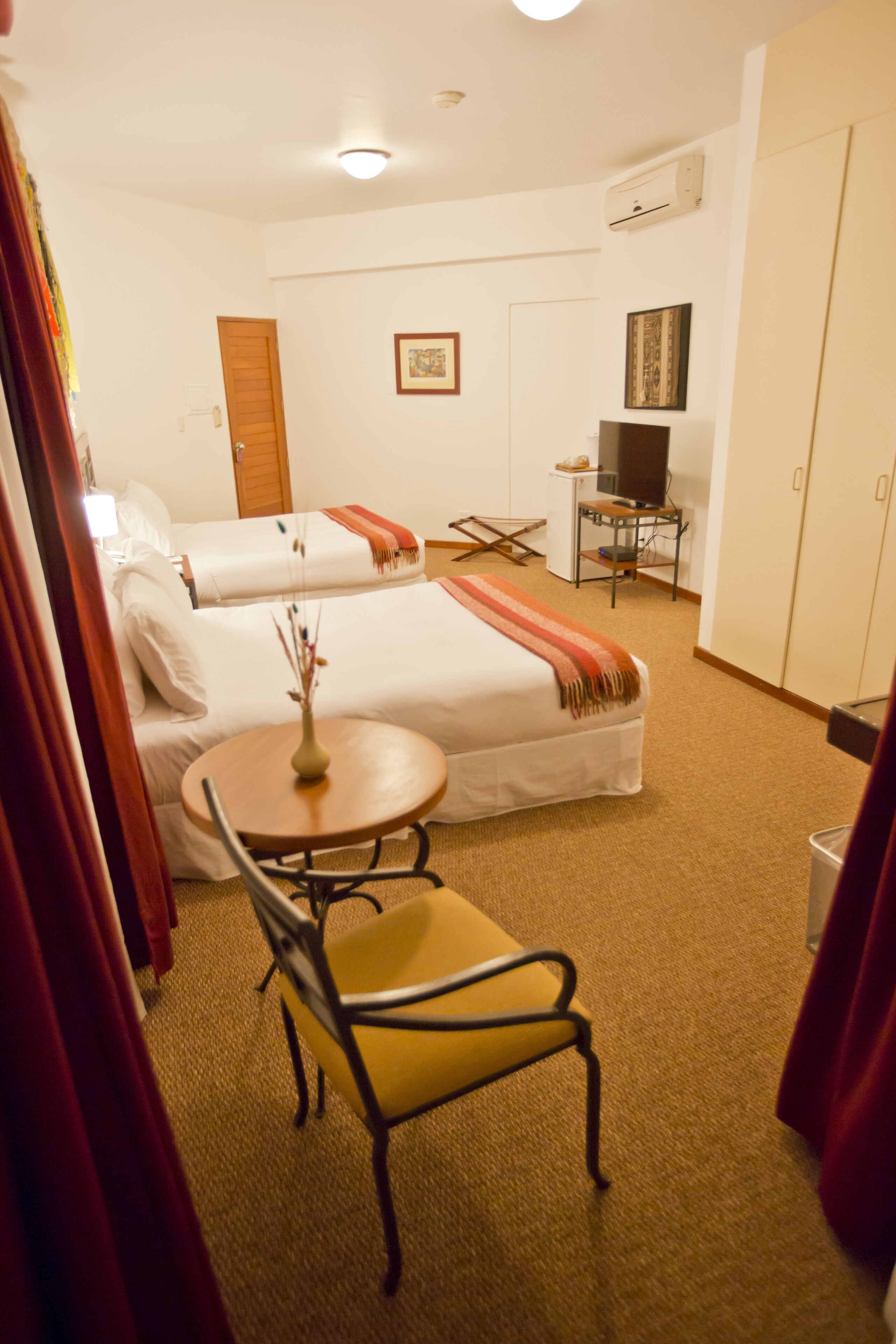 A hotel room with two beds, a small table with a chair, a TV, and a desk with a chair.
