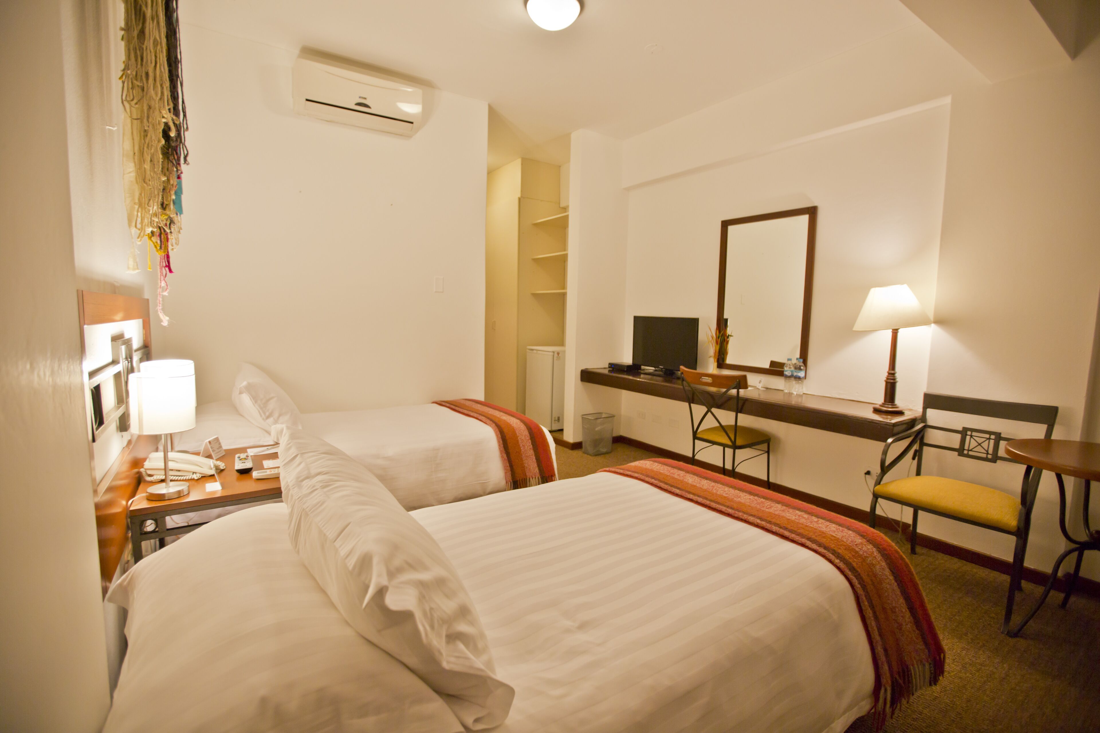 Habitación de hotel con dos camas, un escritorio, una silla, un televisor y un espejo.