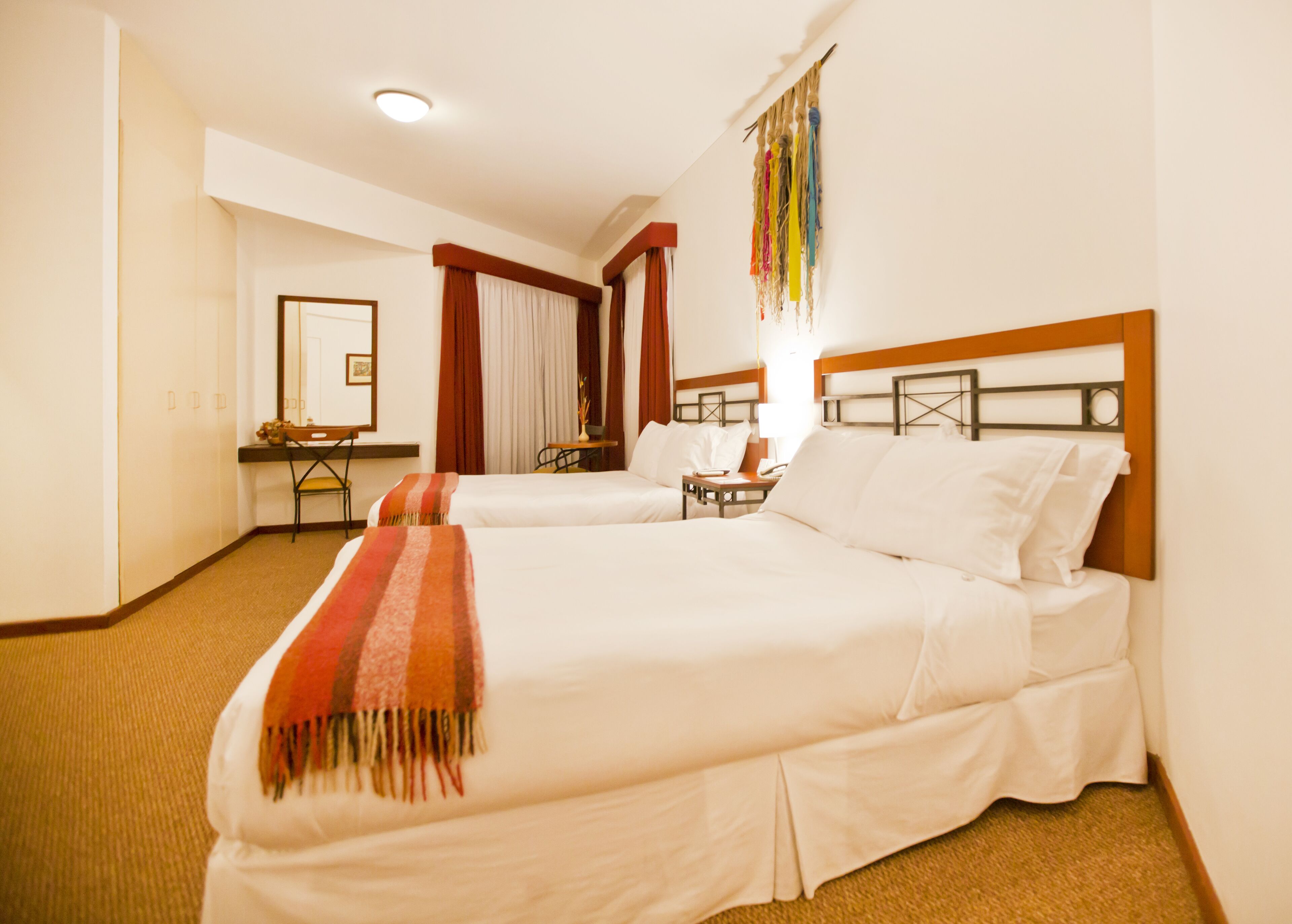 Ein Hotelzimmer mit zwei Betten, einem Schreibtisch, einem Stuhl und einem Spiegel.