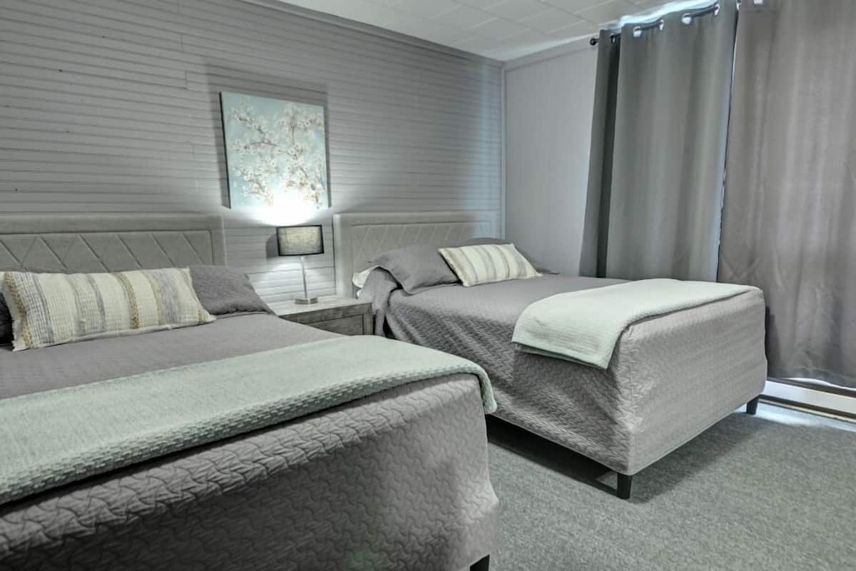 A hotel room with two beds, a nightstand, a lamp, and a window with curtains.