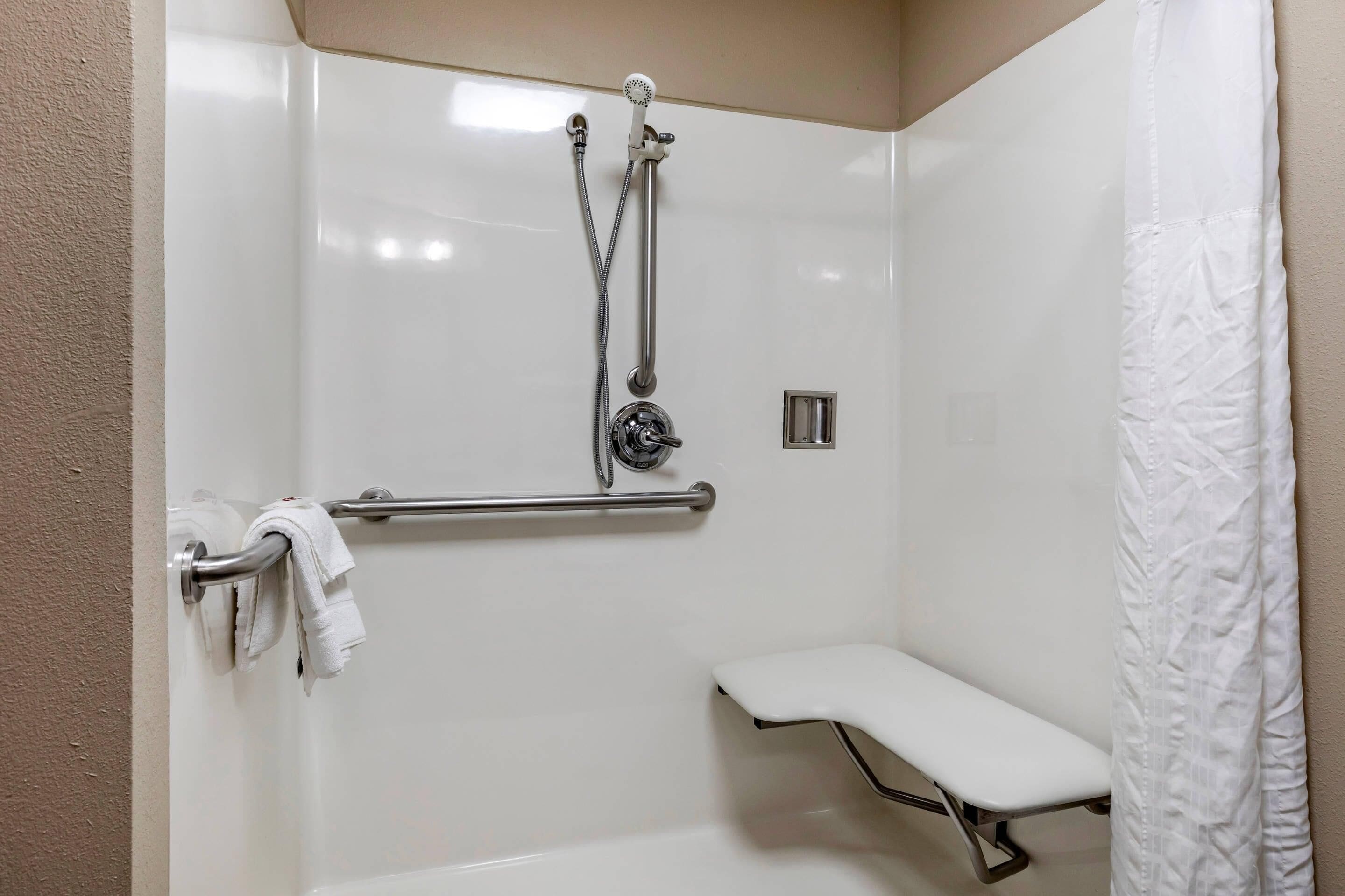 Zona de ducha con barra de apoyo, asiento y toallero.
