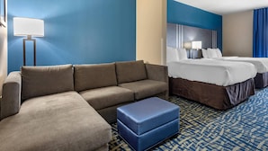 A hotel room with a sofa, a bed, a nightstand, a lamp, and a patterned carpet.