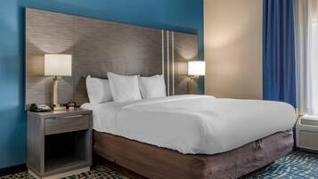 A hotel room with a large bed, two bedside tables with lamps, a telephone, and a small table with a clock.