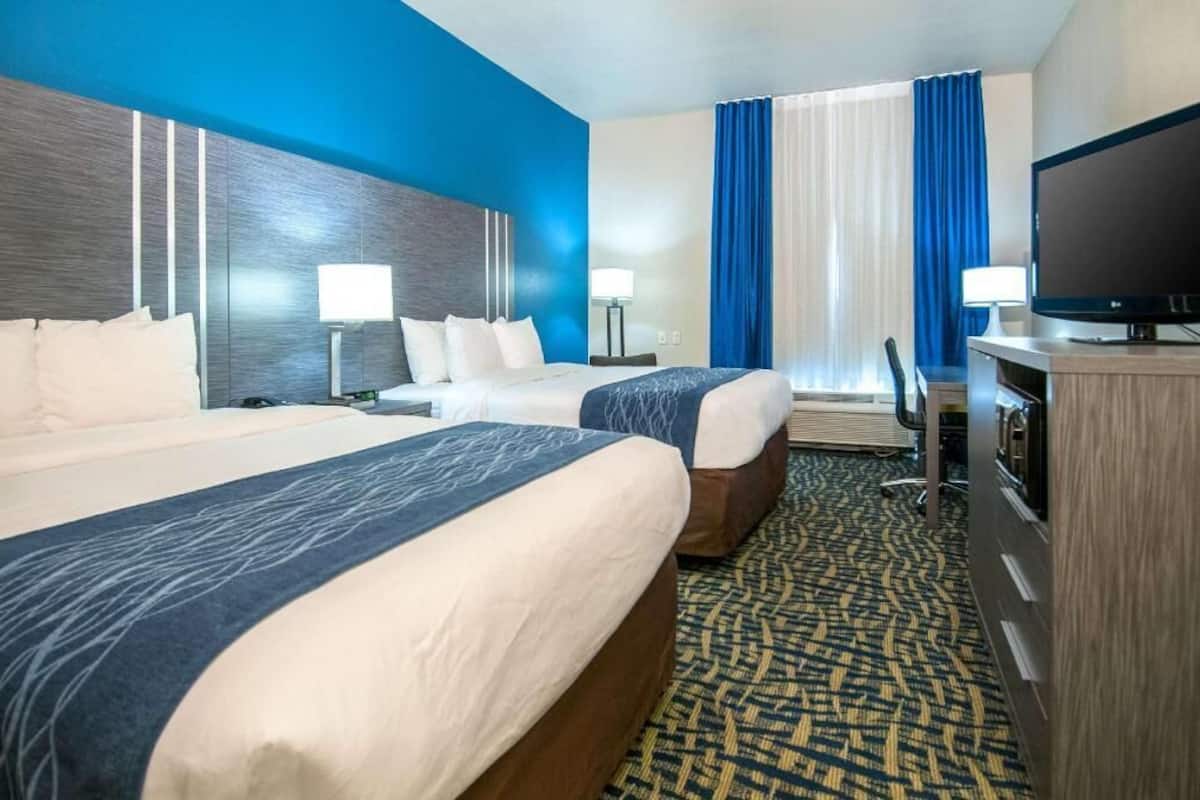 Ein Hotelzimmer mit zwei Betten, einem Fernseher, einem Schreibtisch und einem Fenster mit Vorhängen.