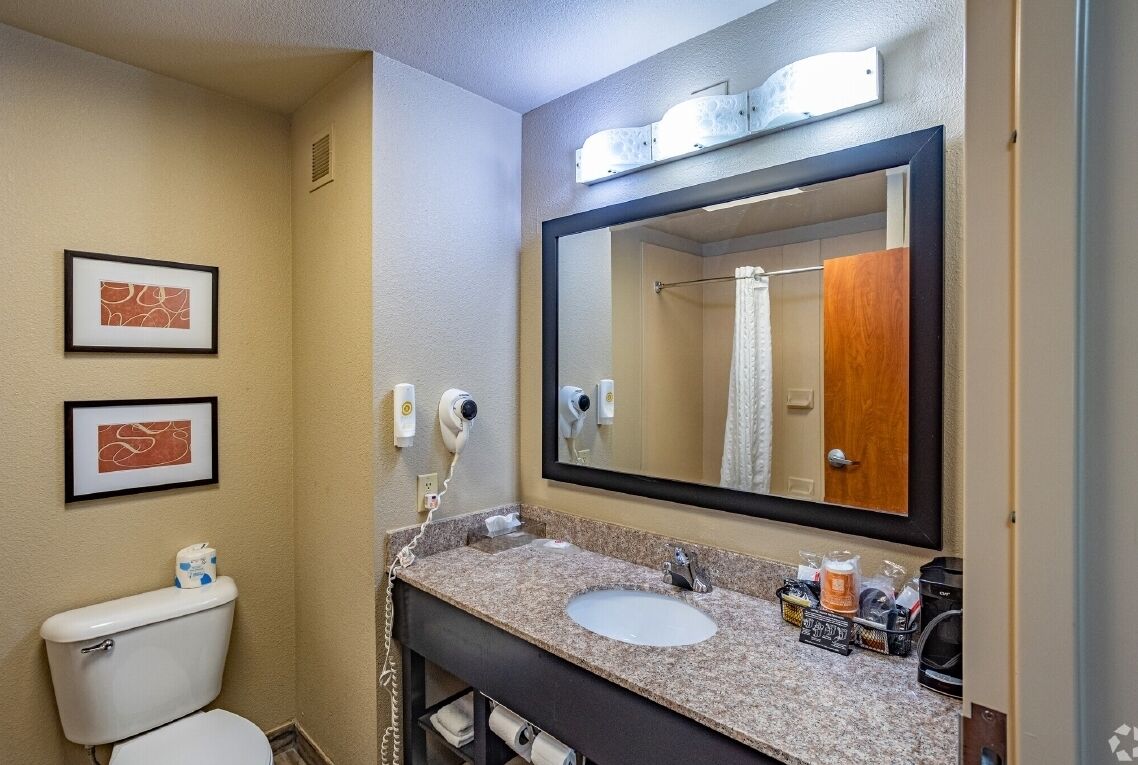 A hotel bathroom with a sink, mirror, toilet, and framed artwork on the wall.