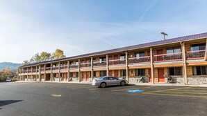 Un motel à plusieurs étages avec un parking, une voiture garée devant et un ciel dégagé.