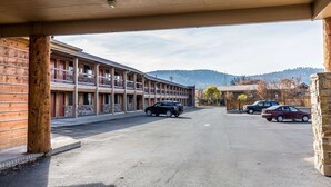 Un motel doté d’un parking couvert, où plusieurs voitures sont stationnées, avec une chaîne de montagnes en arrière-plan.