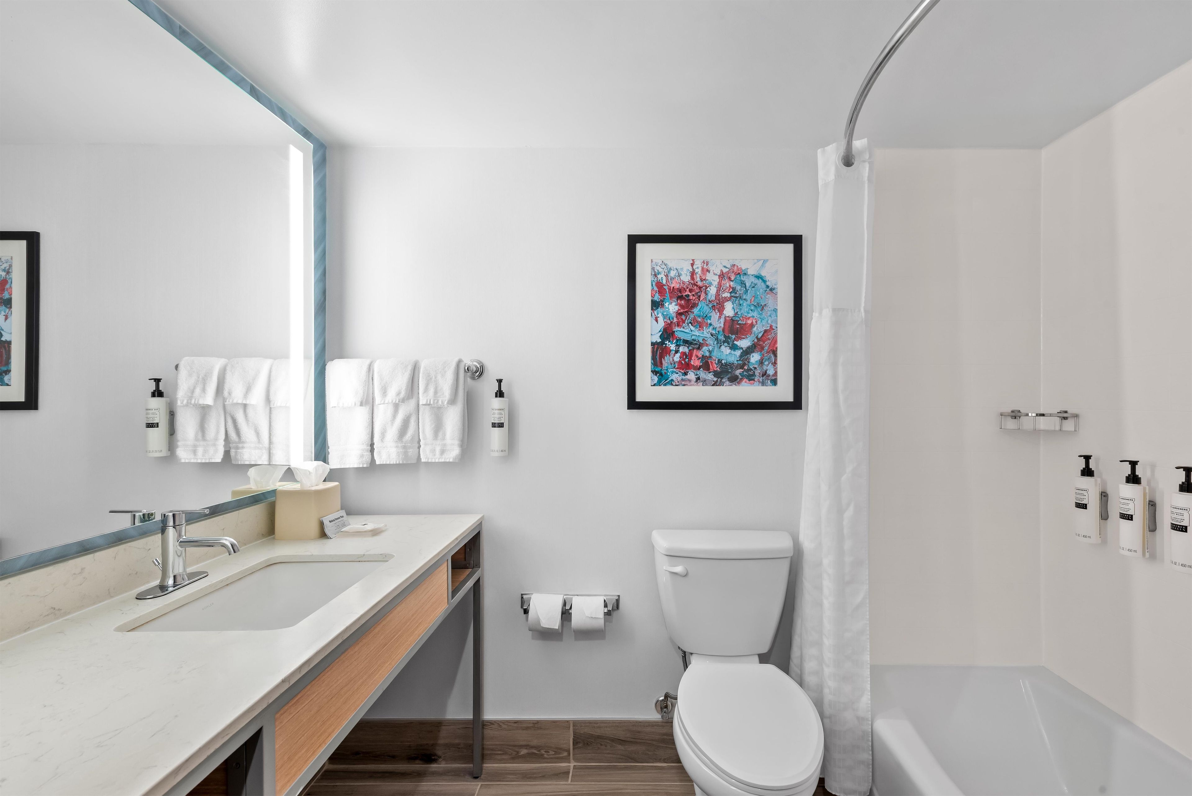 A modern bathroom with a white sink, toilet, and shower area. There are towels and toiletries on the counter.