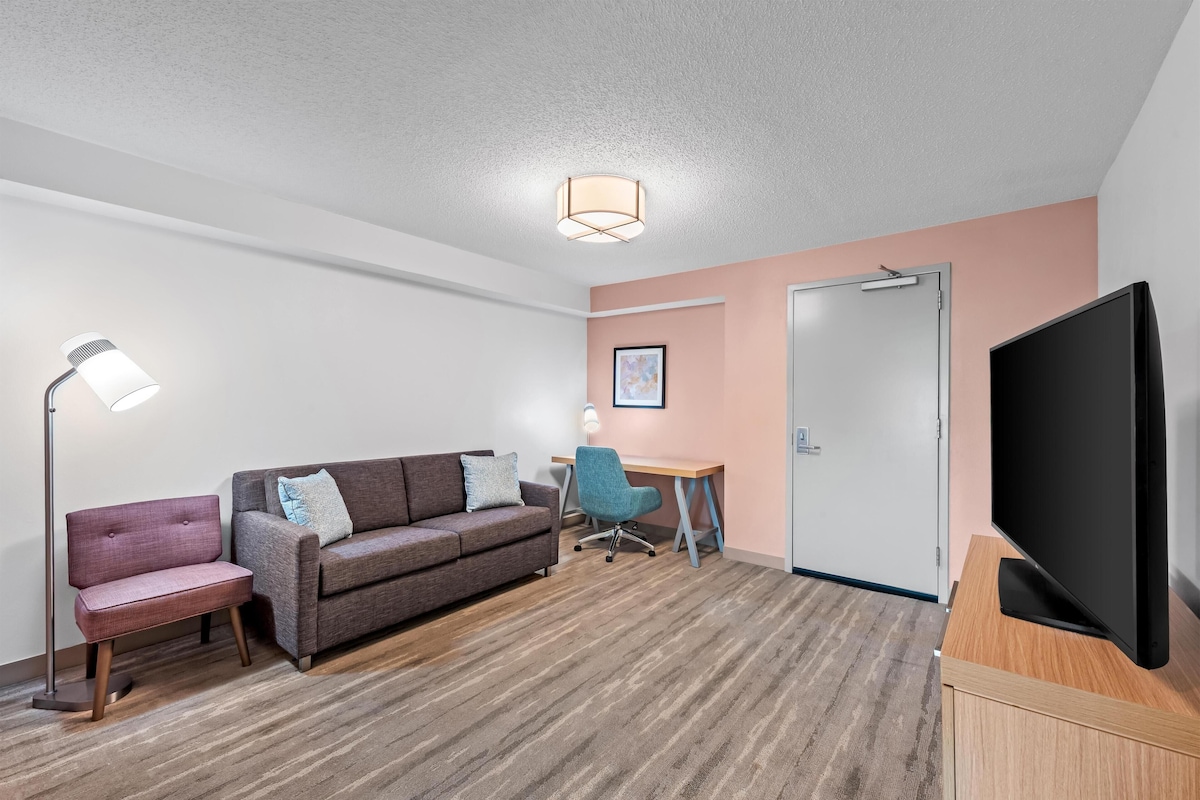 Een hotelkamer met een bank, bureau, stoel, televisie en een deur.