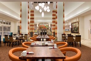 Experience the elegant lobby with a long dining table, vibrant artwork, and ample lighting.