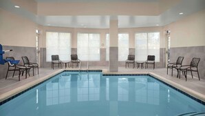 Une piscine entourée de chaises et de tables, de grandes fenêtres et un plafond doté d’un éclairage encastré.
