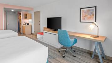 A hotel room with two beds, a desk with a TV, a chair, a desk lamp, and a painting on the wall.