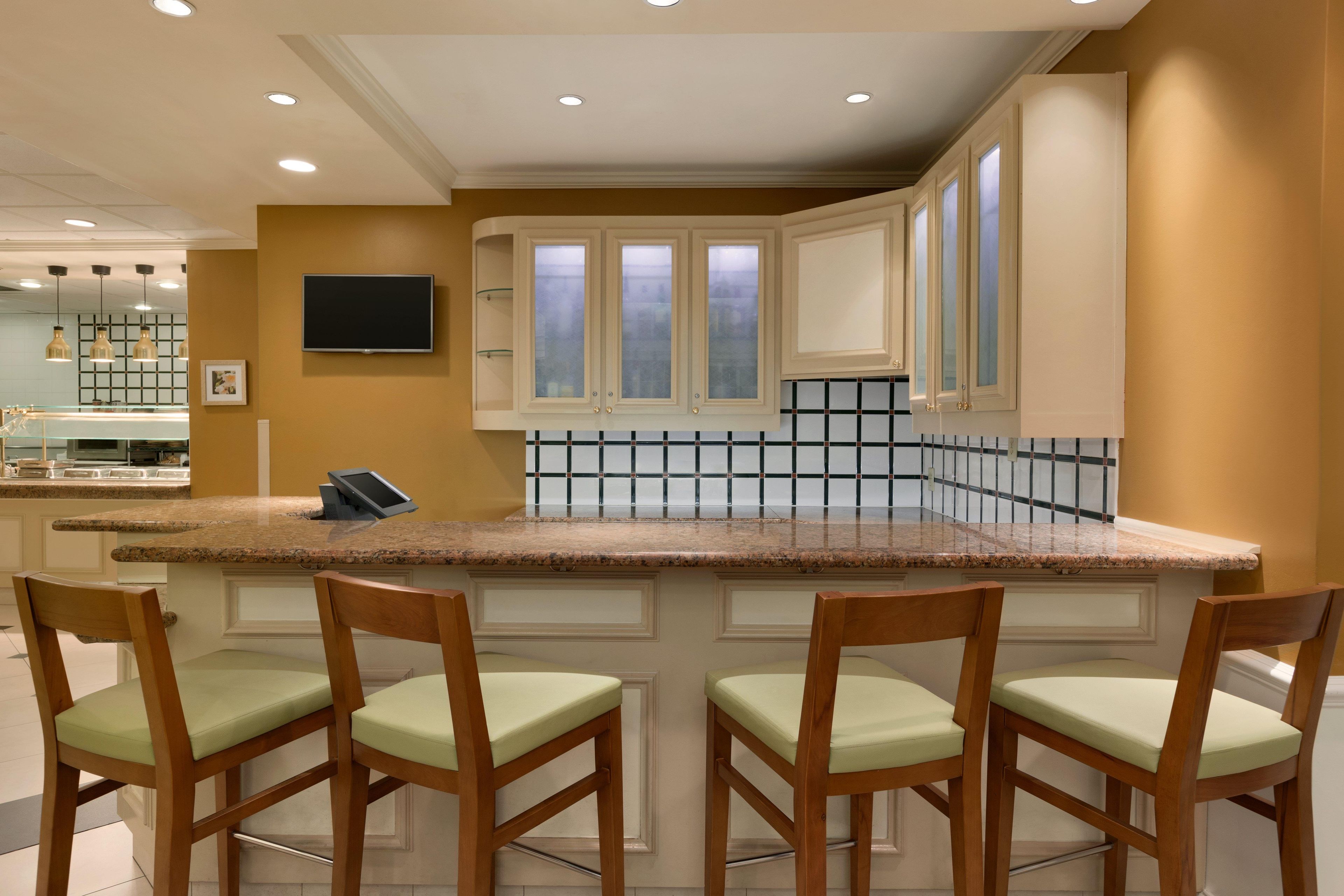 Una cocina con encimera de granito, sillas de madera y salpicadero de azulejos.
