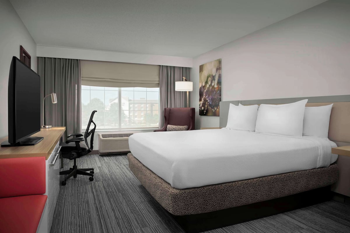 A hotel room with a large bed, a desk with a TV, a chair, and a window with curtains.