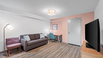A hotel room with a sofa, a desk, a chair, a television, and a door.