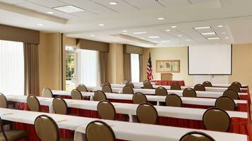 A conference room with multiple tables and chairs, a projector screen, and an American flag.