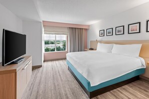 A hotel room with a bed, a TV, a bedside table, a nightstand, a window with curtains, and framed pictures on the wall. - Hilton Garden Inn Fredericksburg (Fredericksburg)