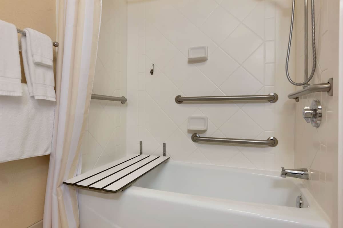 A modern bathroom with a bathtub, grab bars, a showerhead, and a towel rack.