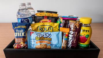 A black tray containing various food items including Pure Life water bottles, Trail Mix, Rold Teddy Grahams, milk chocolate with almonds, and a bottle of apple juice.