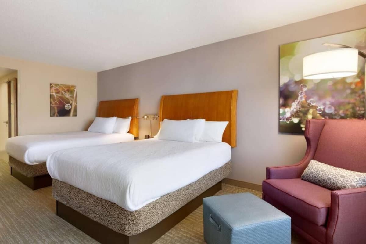 A hotel room with two beds, a chair, and a small table.
