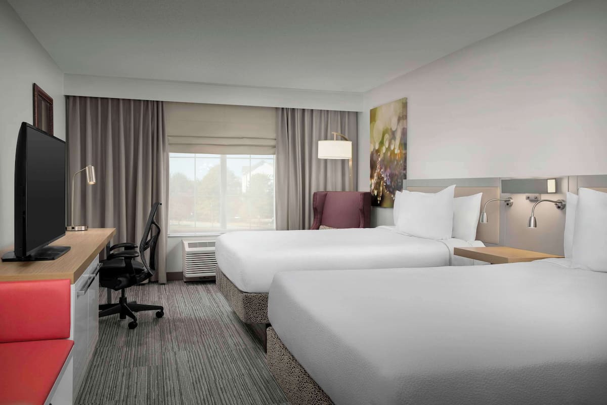 A hotel room with two beds, a desk with a TV, a chair, a lamp, and a painting on the wall.