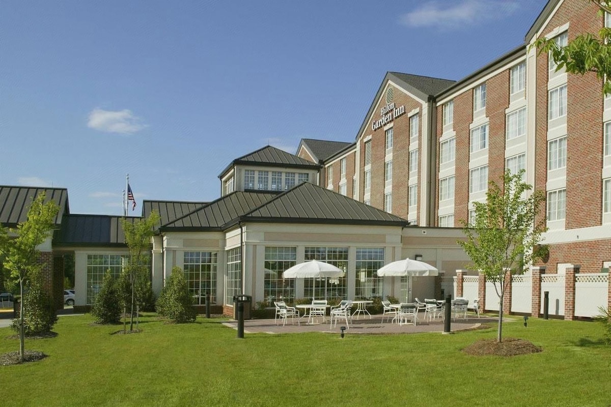 A Hilton Garden Inn hotel with a brick facade, large windows, and outdoor seating area.
