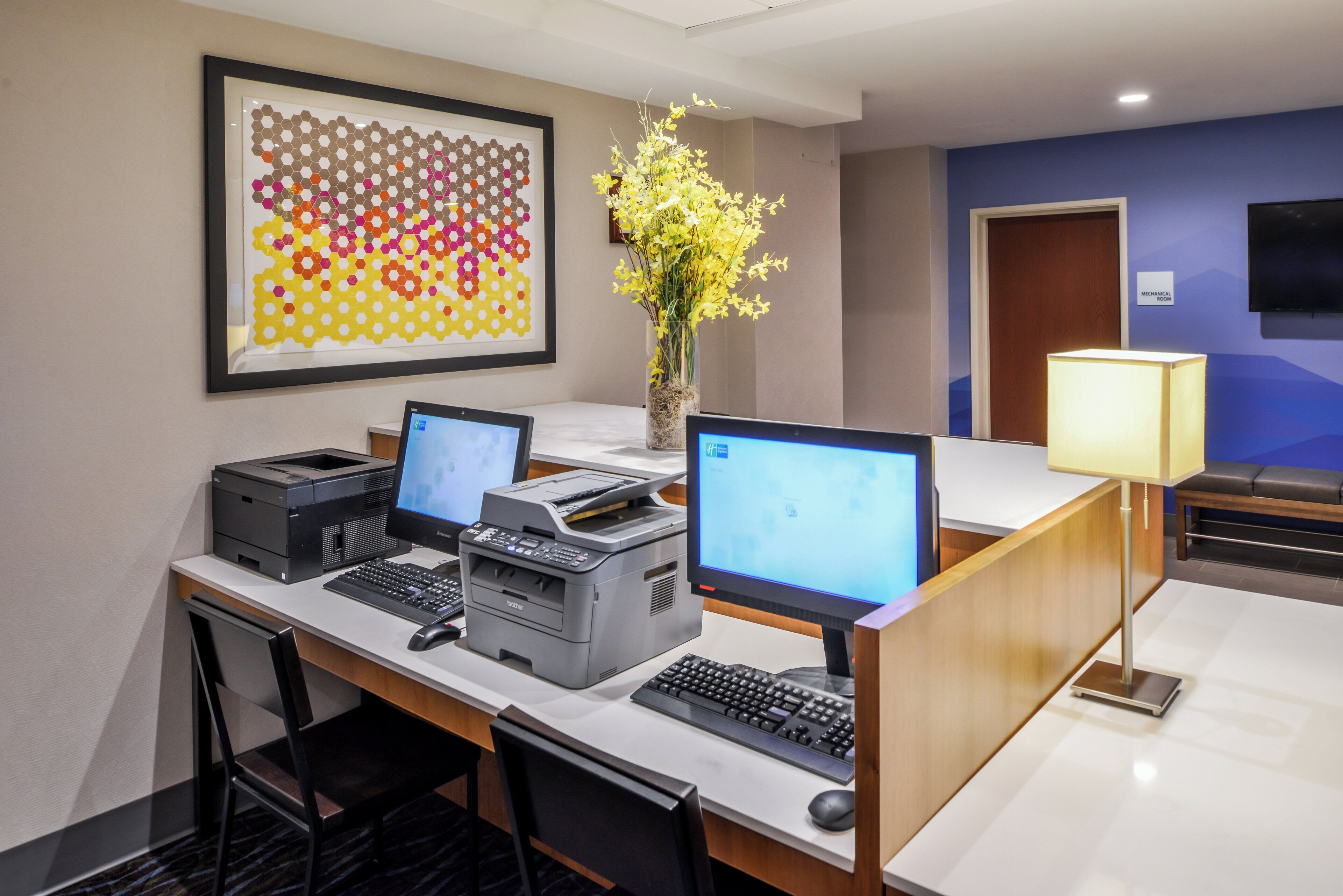 Una reception di hotel con due computer, una stampante e un vaso con fiori gialli.