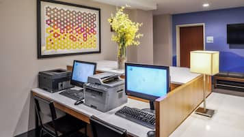 Una reception di hotel con due computer, una stampante e un vaso con fiori gialli.